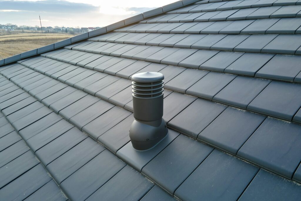 Closeup of ventilation pipe on house roof top covered with ceramic shingles. Tiled covering of
