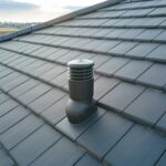 Closeup of ventilation pipe on house roof top covered with ceramic shingles. Tiled covering of
